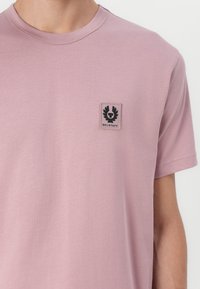 Tricou scurt cu mâneci roz dintr-un amestec moale de bumbac, având o mică emblema neagră pe pieptul stâng. Textură netedă și croi lejer.