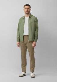 Groene colbert over een witte textuur shirt, gecombineerd met kaki broek en witte sneakers met zwarte accenten.