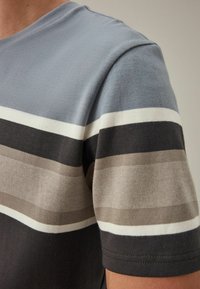Korteærmet stribet t-shirt i lyseblå, grå, hvid og mørkegrå. Har striber med varierende bredder og et blødt, tekstureret stof.