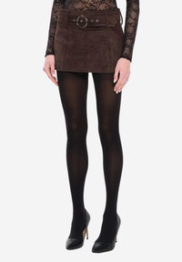 Brązowa mini spódnica ze skóry zamszowej z szerokim paskiem w talii zdobionym okrągłą klamrą, zestawiona z czarnymi rajstopami i obuwiem na wysokim obcasie.