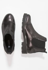 Par de botas Chelsea negras brillantes con superficie texturizada, paneles laterales elásticos y suelas gruesas con dibujo, mostradas desde vistas superior y lateral.