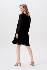 Schwarzes Kleid mit durchsichtigen langen Ärmeln, lockerer Passform und knielangen Saum. Kombiniert mit beigen Blockabsatzsandalen. Einfaches, elegantes Design.