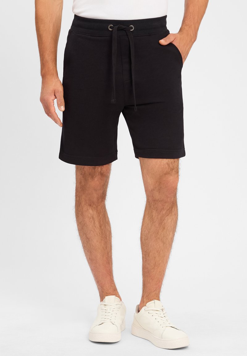 Schwarze Baumwollshorts mit einem elastischen Bund, Kordelzug, Seitentaschen und geradem Schnitt, kombiniert mit weißen Sneakers.