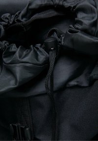 Svart tygdragsäck med samlad topp, flätad snöre och en robust svart plastspärr för stängning. Texturerat material med synliga sömmar.