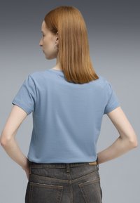 Lichtblauw T-shirt met korte mouwen van zacht materiaal, met een ronde hals en een relaxte pasvorm, gecombineerd met donkerdenim jeans.