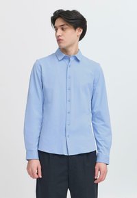 Lichtblauw langemouwhemd met knoopsluiting aan de voorkant, een puntige kraag, een gladde textuur en een slim fit. Gecombineerd met donkere broek.