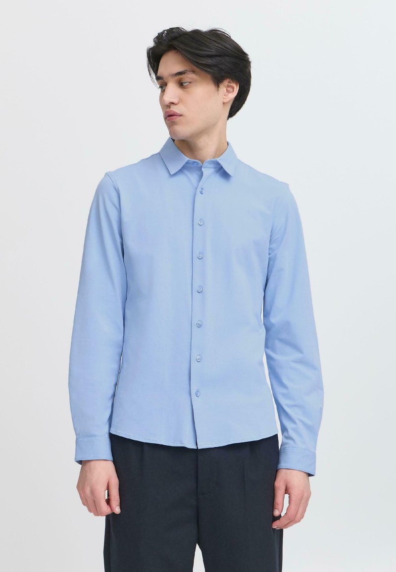 Lichtblauw langemouwhemd met knoopsluiting aan de voorkant, een puntige kraag, een gladde textuur en een slim fit. Gecombineerd met donkere broek.