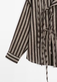 Chemise à manches longues avec des rayures verticales marron foncé et beige, avec des liens en tissu dans le dos et un poignet rayé.