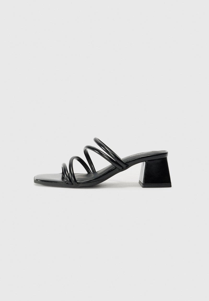 Black heeled sandal with a square toe, featuring three twisted straps on the upper and a chunky square heel. Smooth, glossy material.