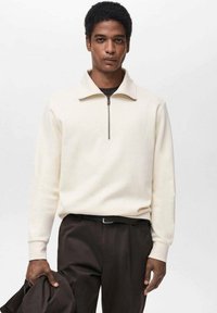 Felpa a zip crema con collo a giro, maniche lunghe, colletto a coste e texture liscia, abbinata a pantaloni scuri. Design minimalista, look moderno.