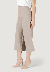 Culottes de color beige claro con un diseño de pierna ancha y textura suave, combinados con zapatos de tacón nude, exhibiendo un aspecto limpio y minimalista.