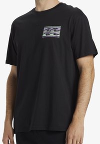 Camiseta negra de manga corta hecha de algodón. Presenta un bolsillo en el pecho con un patrón de olas colorido. Cuello redondo y corte relajado.