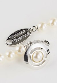 Close-up van een parelketting met zilveren sluiting en ovale plaat gegraveerd met "Vivienne Westwood" op een witte achtergrond.