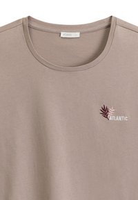 Jasno taupe T-shirt z okrągłym dekoltem i krótkimi rękawami, ozdobiony subtelnym haftem liści w kolorze burgundowym i różowym, z etykietą "ATLANTIC."