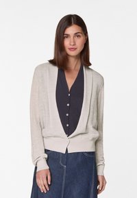 Licht beige cardigan met een zachte textuur, open voorkant en lange mouwen. Draag het over een donker overhemd met knopen en combineer het met een denim rok.