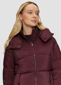 Veste en duvet bordeaux avec un haut col, fermeture éclair, rabat d'épaule à boutons-pression et poches latérales. Texture lisse, design isolé.