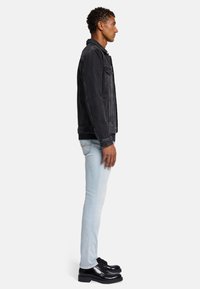 Svart denimjacka med dubbla bröstfickor, bärs över en svart skjorta. Ljusblå slim-fit jeans och svarta snörskor fulländar looken.