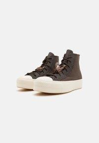 Bruna högstövliga sneakers i texturerat material, med en vit gummikappa på tån, runda snören och en cirkulär logodetalj på sidan.