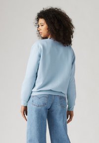 Sweat-shirt bleu clair à coupe décontractée, avec des poignets et un ourlet côtelés ; associé à un jean large bleu clair, présentant un design classique de poche arrière.
