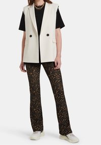 Krémová vesta s dvojitými černými knoflíky, spárovaná s černým tričkem a kostkovanými černobílo-hnědými rozšířenými kalhotami. Bílé tenisky.