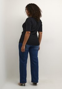 Top negro de manga corta, ajustado a la cintura. Combinado con vaqueros de pierna recta en azul, que presentan una textura de denim clásica, usados con tacones beige.