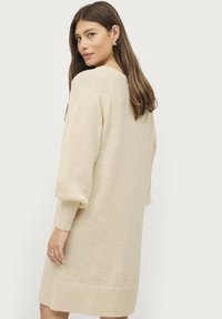 Crèmekleurige gebreide jurk met een relaxte pasvorm, ribgebreide manchetten en zoom. Beschikt over een ronde halslijn en mouwlengte tot halverwege de arm. Zachte textuur.