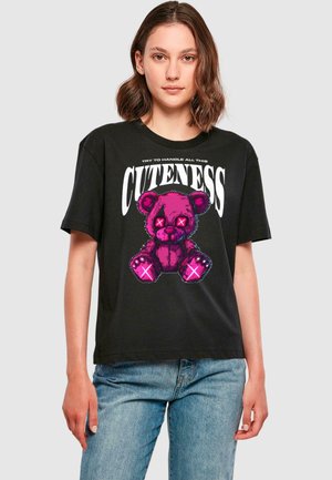 Black short-sleeve T-shirt featuring a cartoon pink teddy bear graphic with X-shaped eyes and the text "TRY TO HANDLE ALL THIS CUTENESS" above.