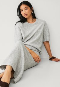 Grå strikket sweater og maxi nederdel sæt, der har kortærmer, en afslappet pasform og blød tekstur. Aksameret med et chunky armbånd og mørke sko.