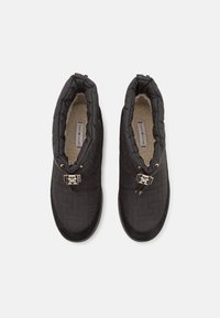 Pár černých prošívaných slip-on bot s polstrovanými límci, zlatými kroužky a fleecem podšitou stélkou na bílém pozadí.