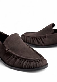 Dark brown suede slip-on shoes with ruffled detailing along the edge and a smooth, rounded toe design. Flat rubber sole.