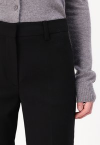 Sorte skræddersyede bukser med flad front og talje. Sammen med en grå ribstrikket sweater med knapdetalje. Glat tekstur.