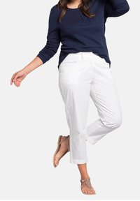 Witte cropped broek met rechte pijpen en zijzakken, gecombineerd met een marineblauwe langemouwenshirt met knoopdetails, en bruine sandalen.