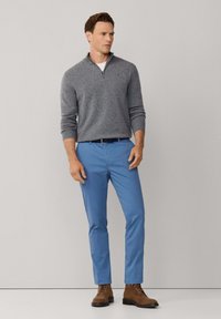 Grijze trui met ritssluiting, lichtblauwe broek en bruine veterschoenen. Glad materiaal met een aansluitend ontwerp, dat een casual stijl uitstraalt.