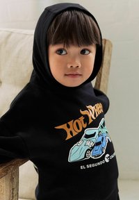 Black hoodie with a front graphic of two cartoon cars in blue and teal, and "Hot Wheels" text in orange. Smooth fabric, relaxed fit.