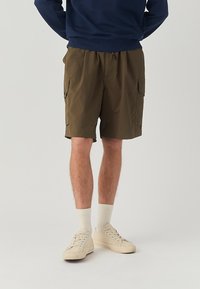 Pantaloni cargo in tessuto verde oliva, con una vestibilità ampia, due tasche laterali e una cintura elastica con cordoncino regolabile.