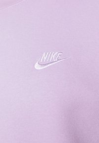 Sudadera de color lavanda hecha de una tela suave, con un logotipo de Nike bordado en blanco en el pecho. Textura suave con un diseño clásico.