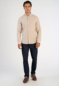 Beige overhemd met knopen en lange mouwen, gecombineerd met donkere broek en bruine bootschoenen. Het overhemd heeft een subtiele structuur en een standaardkraag.