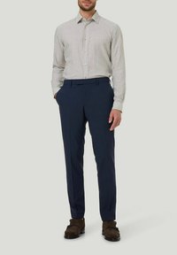 Gestreiftes langärmeliges Hemd in hellbeige und Marineblau, kombiniert mit taillierten Marineblauen Hosen. Die Schuhe sind dunkelbraun aus Wildleder mit einer glatten Textur.