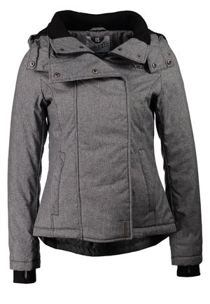 Femme marchant portant une veste grise, un t-shirt gris, un jean bleu, des baskets bleu marine, et portant un sac à dos noir sur une épaule.