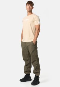 Bézs színű pamut póló fehér grafikával, olajzöld cargo nadrággal és fekete bokacsizmával párosítva. Kényelmes, laza szabás és funkcionális kialakítás.