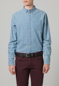 Lichtblauw chambray overhemd met een button-down kraag, een enkele borstzak en lange mouwen, gecombineerd met bordeauxrode jeans en een zwarte riem.