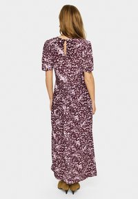 Rochie lungă, violetă, cu mâneci scurte, cu un model floral alb, detaliu cu deschidere în spate și o siluetă fluidă.