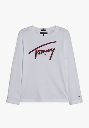 Chemise blanche à manches longues avec texte "Tommy" rouge et noir et petit logo sur la poitrine et le bas de la manche.