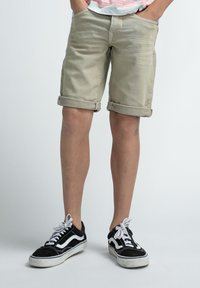 Lichtbeige gerolde shorts van canvasmateriaal, met voorspelden. Gecombineerd met zwarte en witte Vans low-top sneakers.