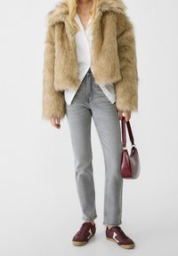 Chaqueta de piel sintética en beige, pantalones vaqueros de mezclilla gris, zapatillas burdeos con detalles en crema y un pequeño bolso burdeos de textura suave.