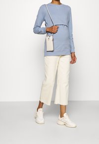 Felpa azzurra chiara in morbido tessuto, abbinata a pantaloni bianchi cropped con orlo sfilacciato. Sneakers bianche e una piccola borsa a tracolla.