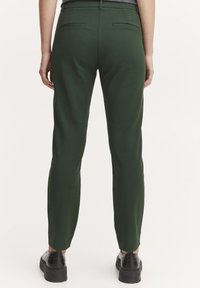 Grønne skræddersyede bukser med slim fit, som har to baglommer og en glat tekstur, parret med sorte platform sko.