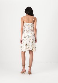 Rochie de vară cu flori, cu bretele subțiri ajustabile, o fustă volanată și un fundal crem deschis. Prezintă modele colorate de flori pe toată suprafața.