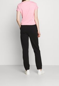 Rosa T-Shirt mit kurzen Ärmeln, kombiniert mit schwarzen Jogginghosen. Die Hosen haben elastische Bündchen und Seitentaschen. Weiße Turnschuhe runden das Outfit ab.