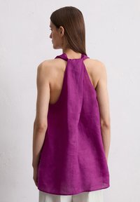 Haut halter en lin violet avec un dos ouvert et des liens au cou, présentant une coupe ample et une texture lisse et légère.